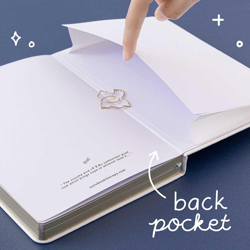 Open back page pocket of Tsuki ‘Suzume’ Winter Limited Edition Bullet Journal held in hand with free bookmark gift on navy background