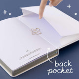 Open back page pocket of Tsuki ‘Suzume’ Winter Limited Edition Bullet Journal held in hand with free bookmark gift on navy background
