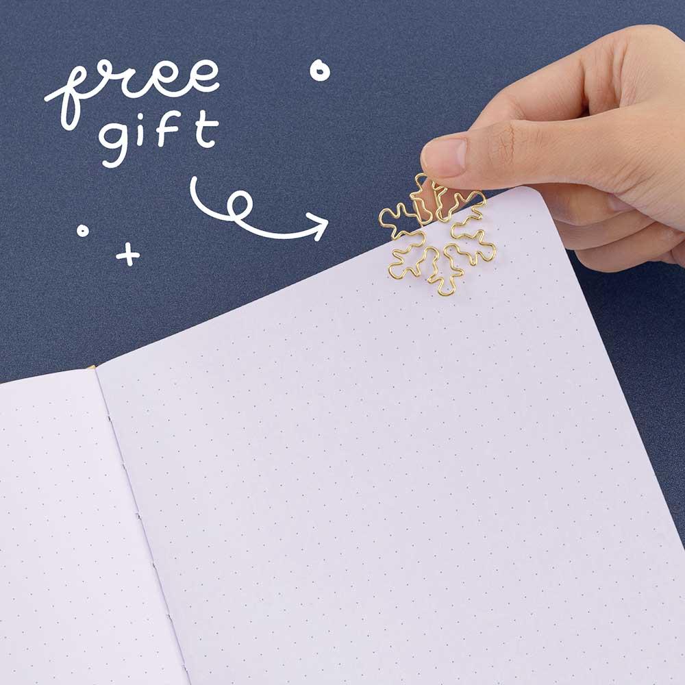 Close up of open page of Tsuki ‘Winter Journey’ Limited Edition Bullet Journal with free bookmark gift held in hand on navy background